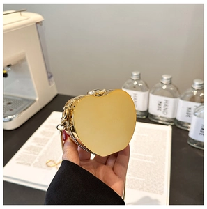 Close-up of heart-shaped gold acrylic evening bag with chain held in hand