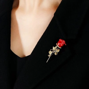 Detailed close-up of a red rose brooch with gold leaves on a black blazer lapel