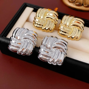 Detail view of square woven knot earrings in gold and silver finish inside a jewelry box