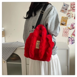 Detail of red plush tote bag with gold metal buckles and a black adjustable strap
