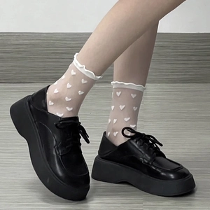 Gros plan sur des chaussettes en tulle blanc à cœurs avec des chaussures compensées noires