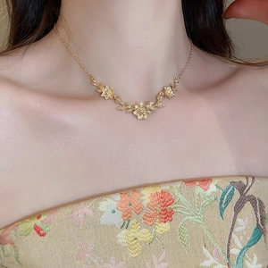 Close-up of golden floral leaf pendant necklace with crystals on a woman's collarbone