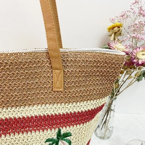 Detail of woven straw tote bag with palm tree embroidery and brown leather handles