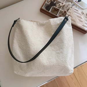 Detailed embroidery on a beige cotton tote bag with a black leather shoulder strap