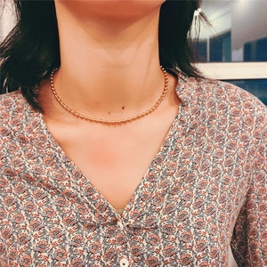 Close-up of a gold titanium ball chain necklace worn by a model on the collarbone