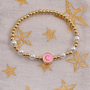 Detail of beaded gold and pearl bracelet with a pink enamel letter C moon charm