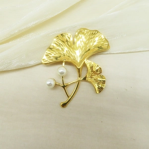 Detailed view of gold ginkgo leaf brooch with twin pearls on elegant satin fabric