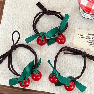 Close-up of three cherry hair ties with red beads and green ribbon bows on linen
