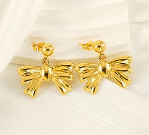 Close-up of golden bow-knot earrings with polished metallic finish on a white pedestal