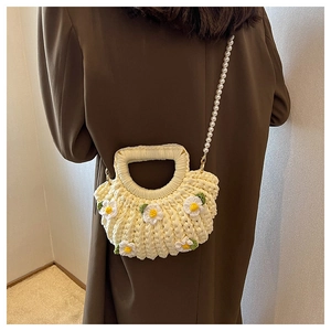 Detail of a beige woven shell bag featuring white daisy accents and a pearl chain strap