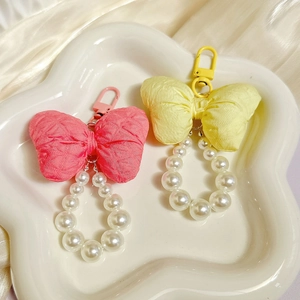 Close-up of pink and yellow fabric bow keychains with imitation pearls on ceramic tray