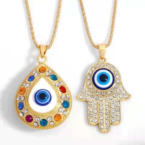 Detail of Hamsa Hand and teardrop Evil Eye pendants with colorful crystals and gold chain