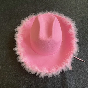 Sombrero vaquero rosa con corona y plumas sobre una superficie oscura brillante