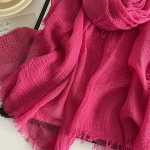 Close-up detail of rose red linen scarf showing crinkle texture and fringe edges
