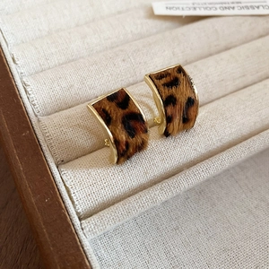 Close-up of leopard print C-shape earrings with gold edges on a cream velvet tray