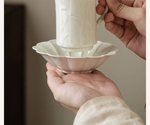 Detail of white ceramic teacup with bamboo relief being held in a petal-shaped saucer