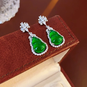 Close-up of green gourd earrings with white zircons on a brown leather jewelry box
