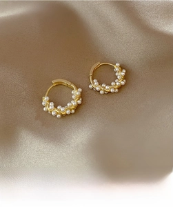 Detailed close-up of golden geometric hoop earrings with embedded white pearls on satin