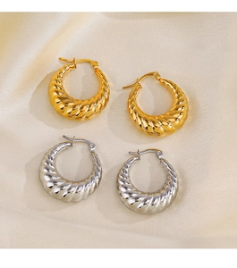 Gros plan de boucles d'oreilles torsadées dorées et argentées sur tissu en soie beige