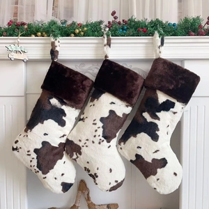 Three plush cow print Christmas stockings hanging on a white fireplace mantel