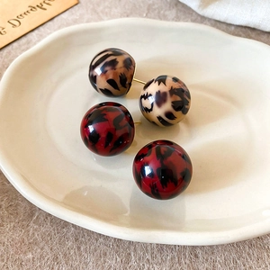 Detailed macro view of round resin leopard print stud earrings in red and tan on ceramic