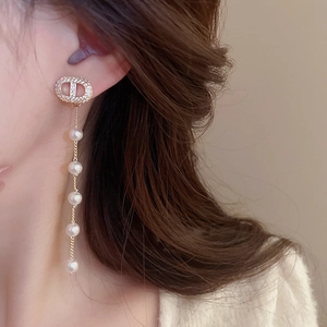 Close-up of dangling gold tassel earrings with pearls and rhinestone letter accents