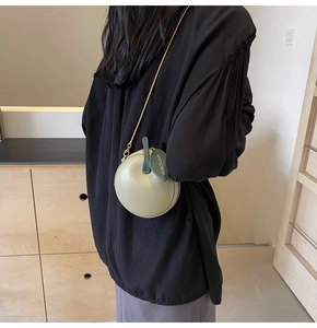 Close-up of light green apple-shaped bag with gold chain and leaf pendant detail