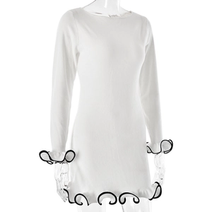Close-up of wavy ruffled cuffs and black contrast trim on white long sleeve knit dress