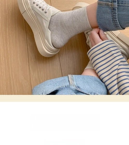 Close-up of light grey ribbed knit ankle socks worn with white sneakers on wood floor