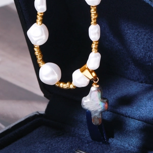 Vue détaillée du collier de perles baroques avec croix en nacre sur velours bleu