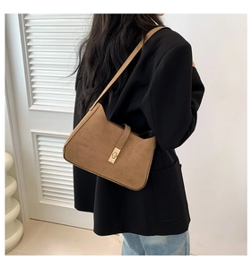Brown suede crescent hobo bag with gold buckle shown on shoulder of model in black suit
