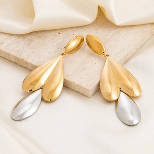 Detail of two-tone gold and silver leaf earrings displayed on a beige stone surface