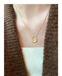 Close-up of a minimalist gold U-shaped pendant necklace worn on a brown knit sweater