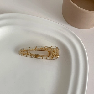 Macro shot of acetic acid hair clip with gold foil flakes on a white ceramic tray