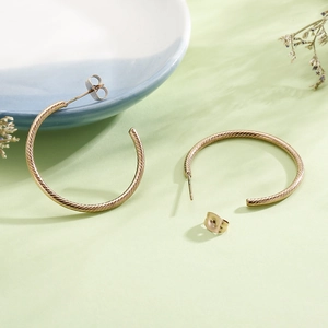 Detailed close-up of golden twisted texture C-shaped hoop earrings on aesthetic background