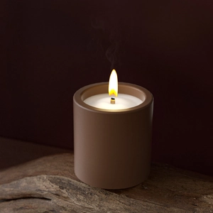 Close-up of a burning candle in a matte brown cylinder resin jar on a rustic wood base