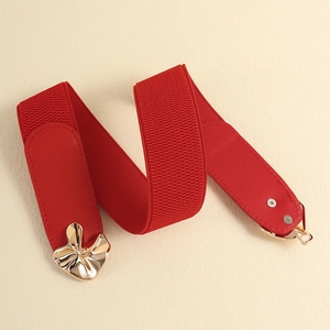Detail of red elastic waist belt featuring a gold floral metal buckle on a textured surface