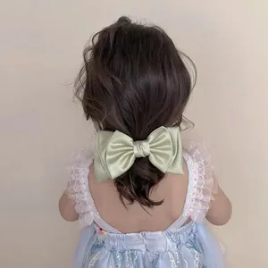 Detail of a light green satin bow hair clip on a young girl's hair with a soft sheen
