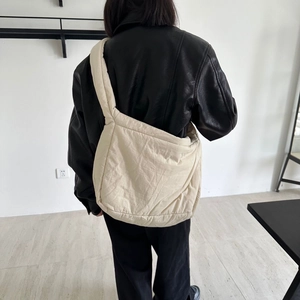 Model wearing a puffy beige crossbody tote bag with wide strap over a black jacket