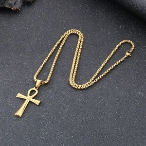 Macro shot of gold Ankh cross pendant with box chain on dark textured surface