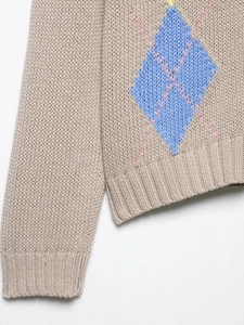 Détail d'un pull en maille à losanges avec poignets côtelés bleus et roses