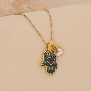 Detail of a golden Hamsa hand necklace featuring a green enamel palm and white heart charm