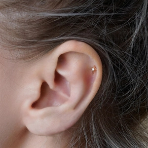 Detailed view of a gold star stud earring with a small diamond on a model ear