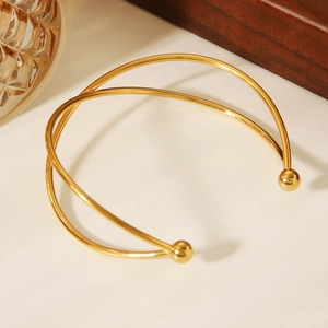 Detail of minimalist 18k gold cross-line open bangle with polished finish and ball ends
