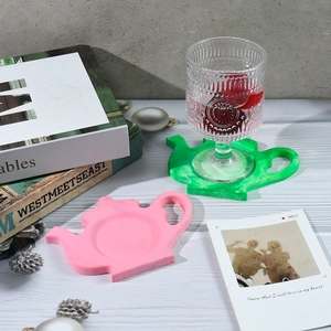 Detail of teapot-shaped silicone coasters in pink and green on a white wooden table