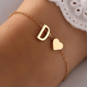 Bracelet doré élégant avec lettre D et pendentif cœur porté au poignet avec dentelle blanche
