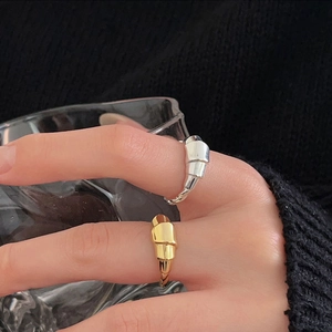 Close-up of gold and silver croissant twist rings worn on a hand with a glass