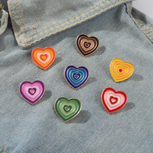 Detailed view of seven colorful heart-shaped gradient enamel brooches on denim jacket