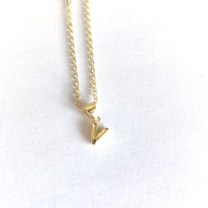 Close-up of a minimalist gold V-letter pendant on a fine chain over a white background