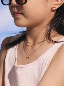 Détail d'un enfant portant un collier doré multicouche et des boucles d'oreilles cœur